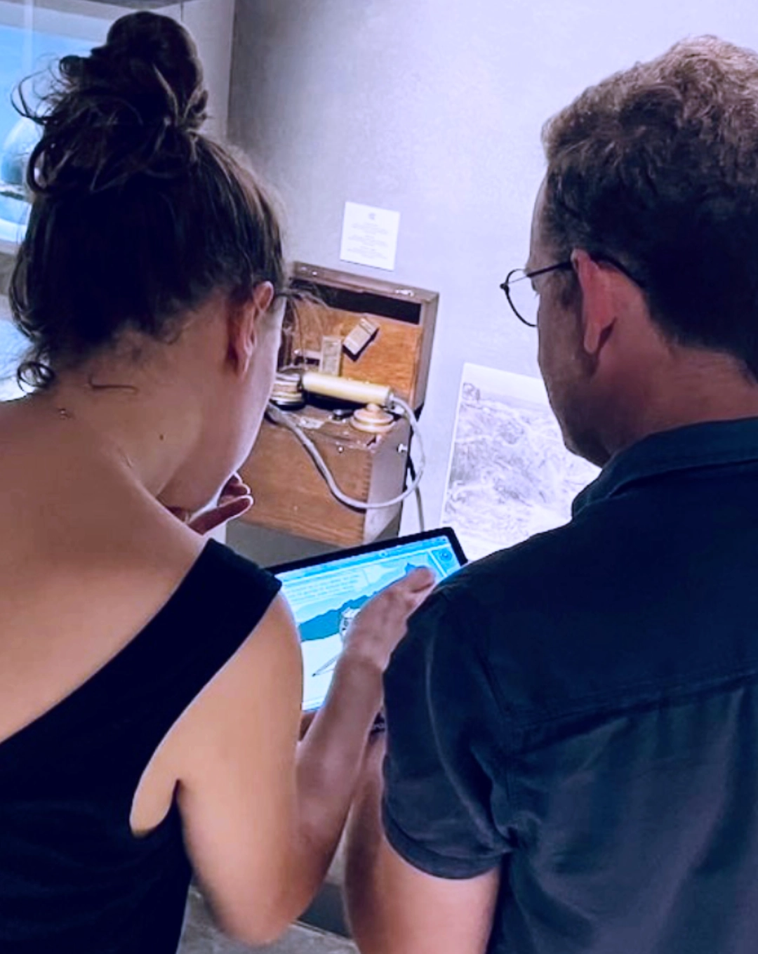 Participants en train de coopérer autour d’une tablette pour résoudre une énigme historique dans un jeu d’enquête immersif au sein d’un centre d’interprétation.